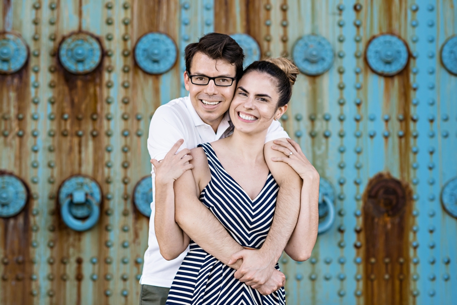 A man hugs his fiance in front of blue and orange doors.
